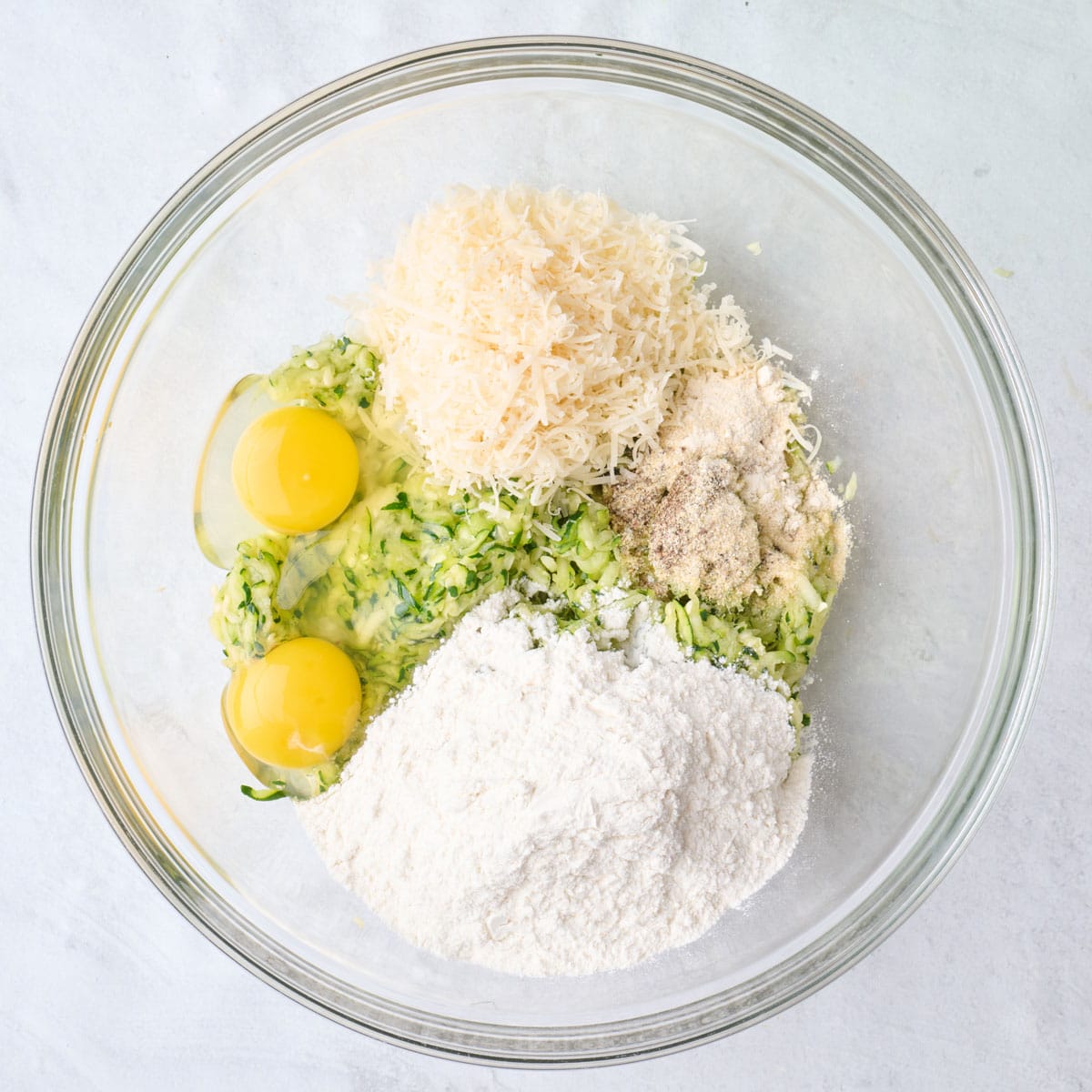 Shredded zucchini in a bowl with egg, flour, parmesan, and seasonings.