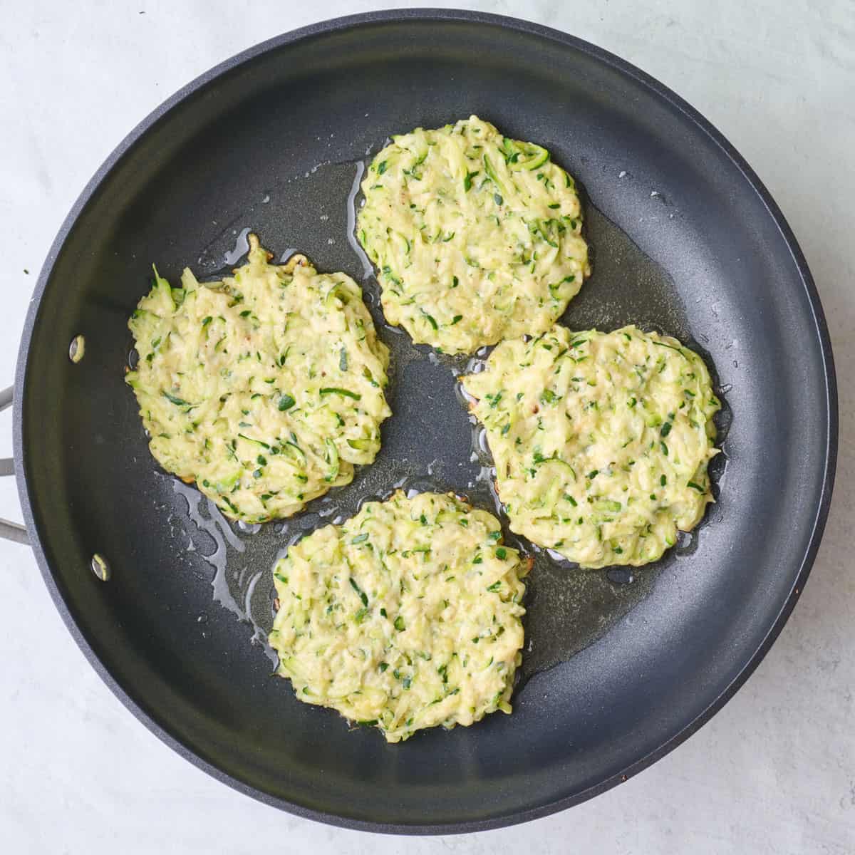 4 zucchini fritters in a skillet.