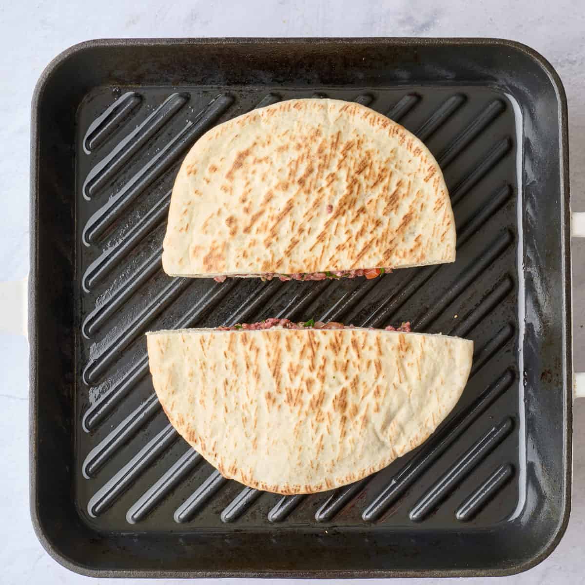 Meat stuffed pita halves on a grill pan.