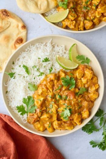 Curry chicken with coconut milk served in a bowl on the side of rice with naan nearby.