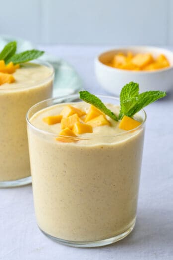 Homemade mango smoothie in small glasses topped with extra diced mango and fresh mint.