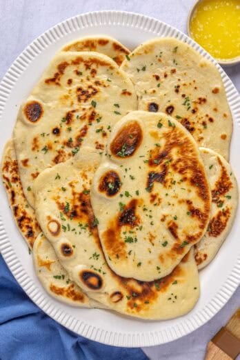 Naan served on a platter, garnished with parsley with a small dish of melted butter nearby.