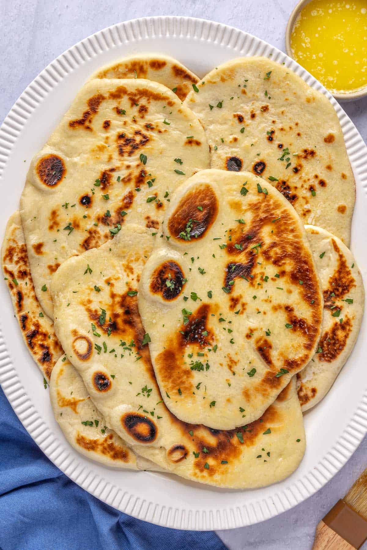 Naan served on a platter, garnished with parsley with a small dish of melted butter nearby.