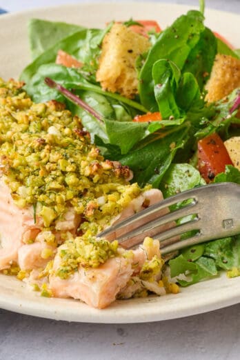 Best pistachio crusted baked salmon filet on a plate with a fork breaking off a piece.