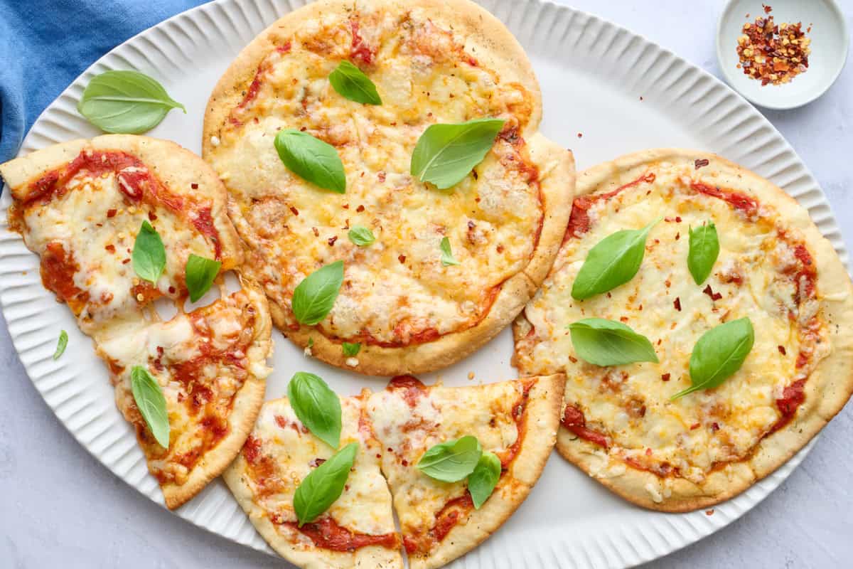 Easy pita pizzas on a platter topped with fresh basil, one cut into quarters.