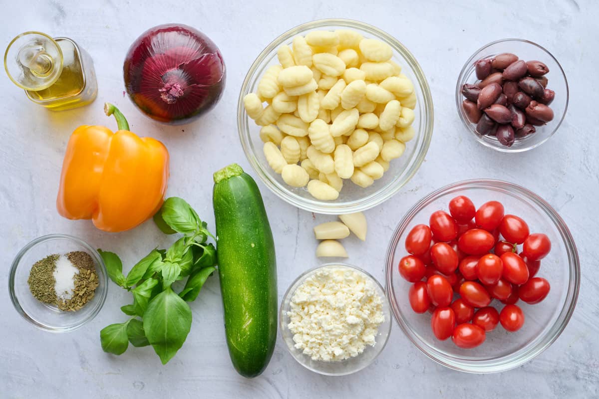 Ingredients for recipe: oil, red onion, bell pepper, seasonings, basil, zucchini, garlic, gnocchi, feta cheese, olives, and cherry tomatoes.