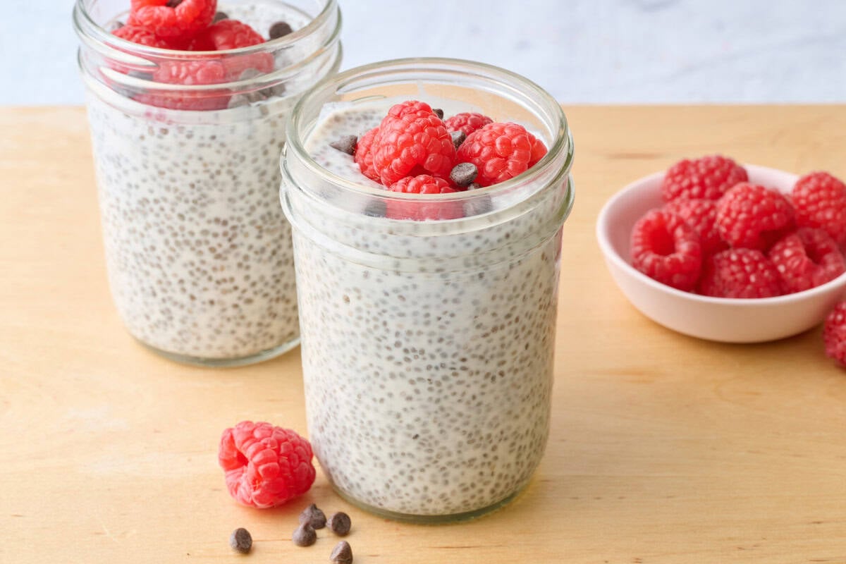 2 Yogurt chia pudding in jar, focus on one, topped with fresh diced strawberries with small spoon nearby, extra fresh fruit nearby.