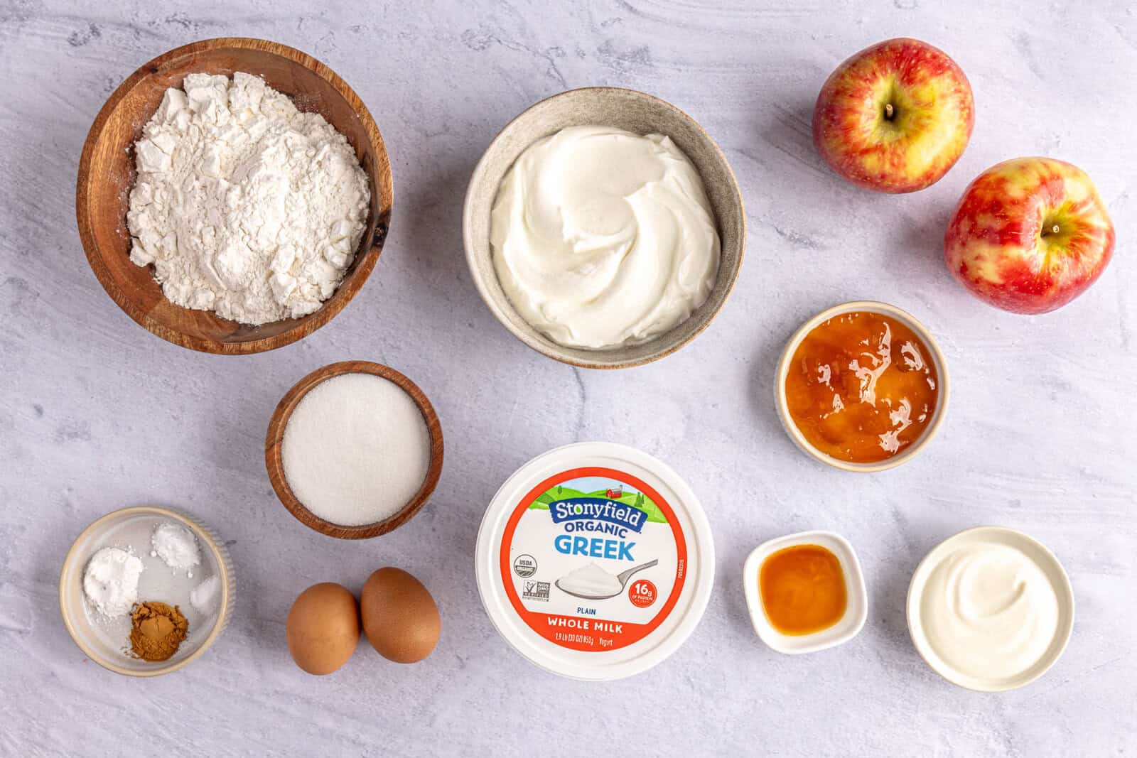 Ingredients for cake recipe before prepping: Stonyfield Organic Whole Milk Greek Yogurt, flour, sugar, cinnamon, baking powder, baking soda, salt, eggs, vanilla, apricot jam, and apples.