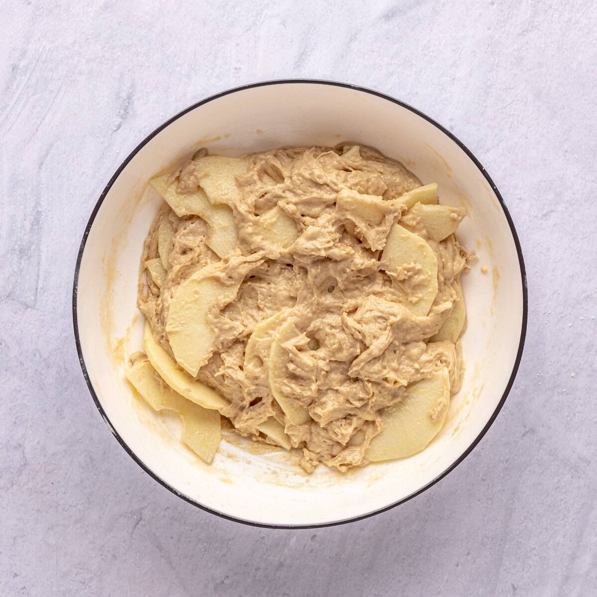 Apple yogurt cake batter mixed in a bowl with thin sliced apples.