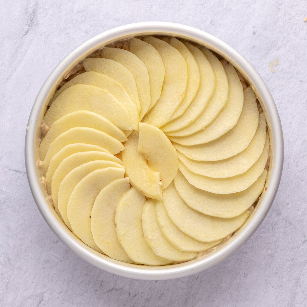 Cake batter for recipe in a cake pan with apple slices on top before baking.