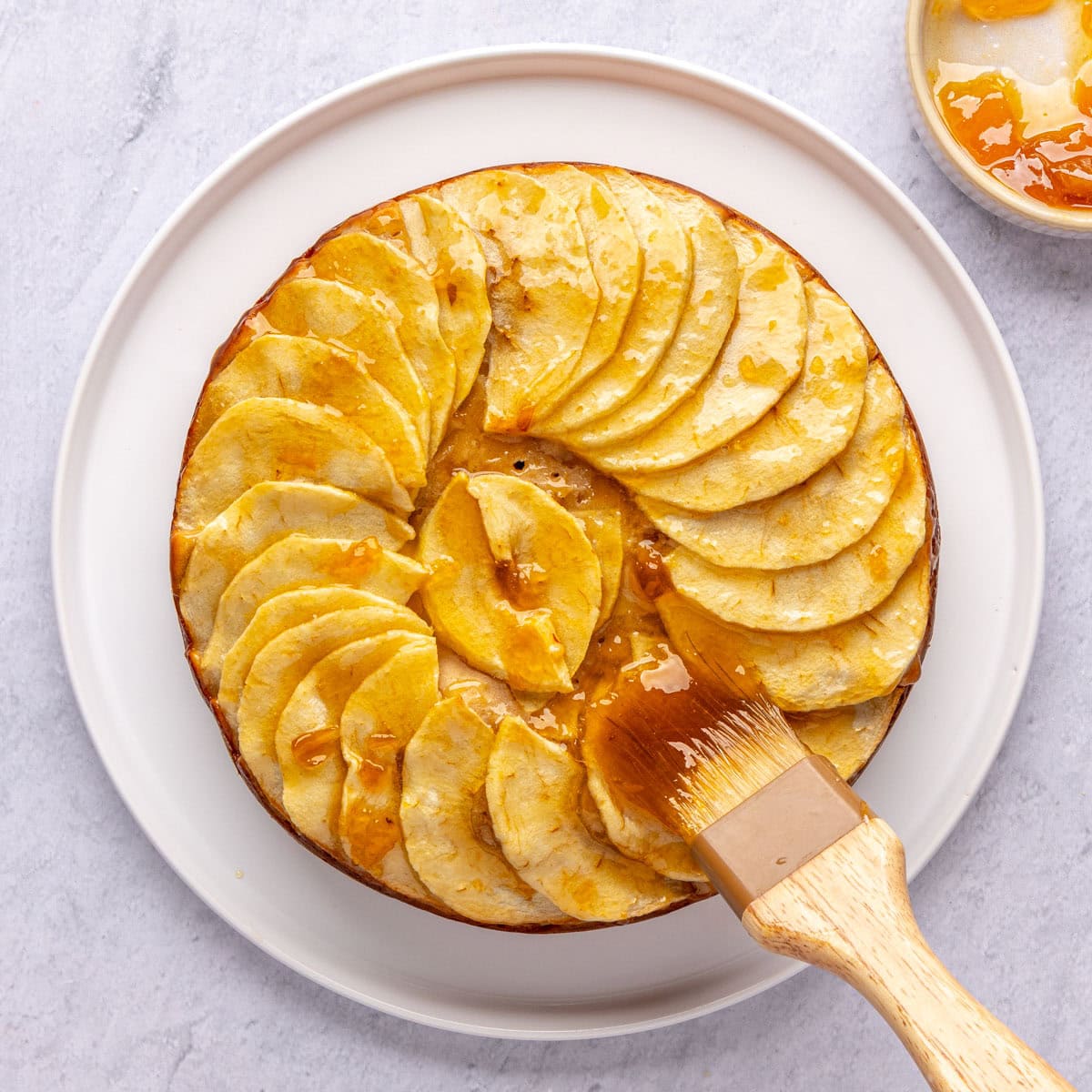 Pastry brush brushing apricot jam over apple yogurt cake after baking.
