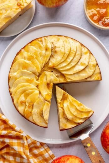 Apple cake with Greek yogurt on a platter with a slice cut away, topped with apricot jam.