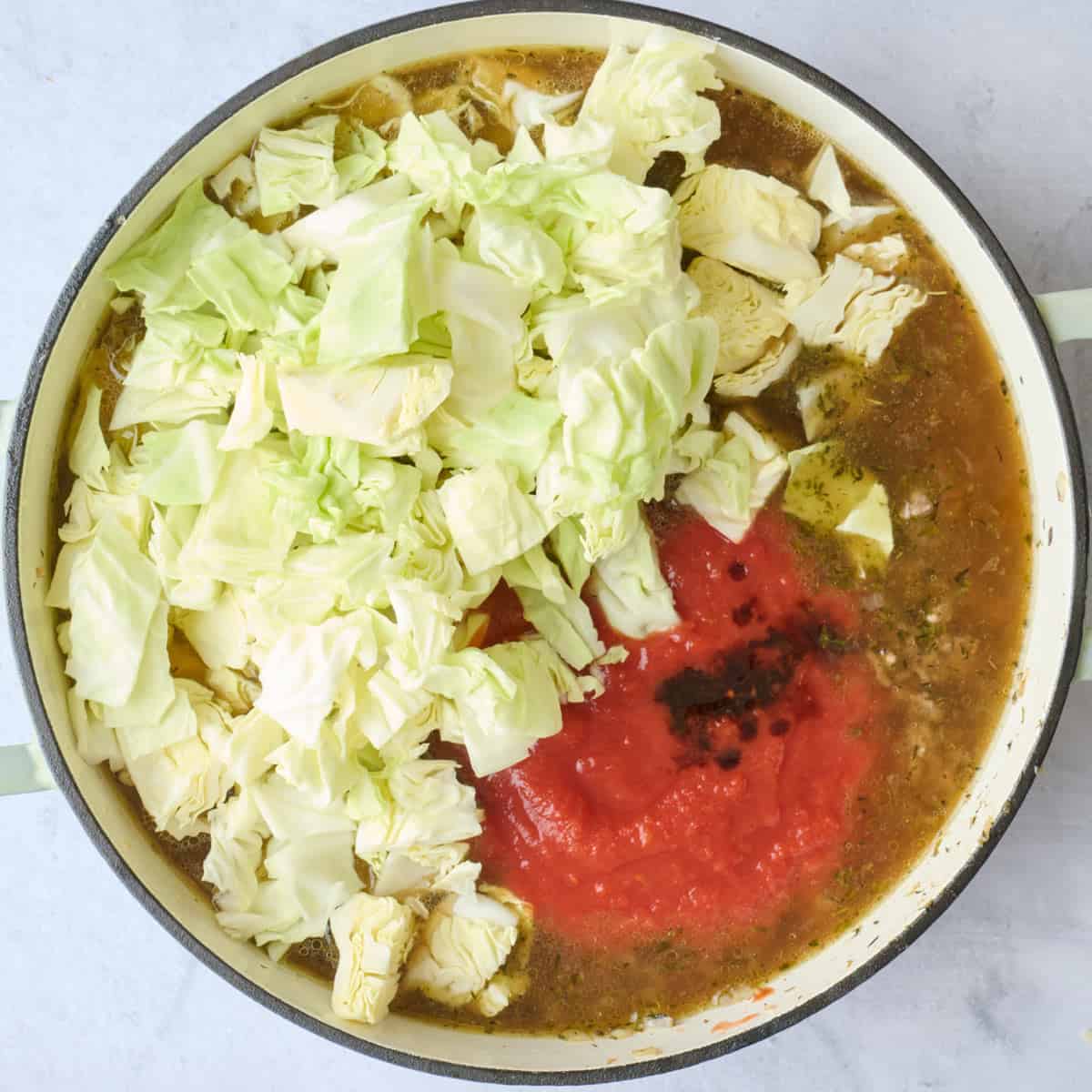 Chopped cabbage, tomatoes, sauce and broth added to pot with ground beef.