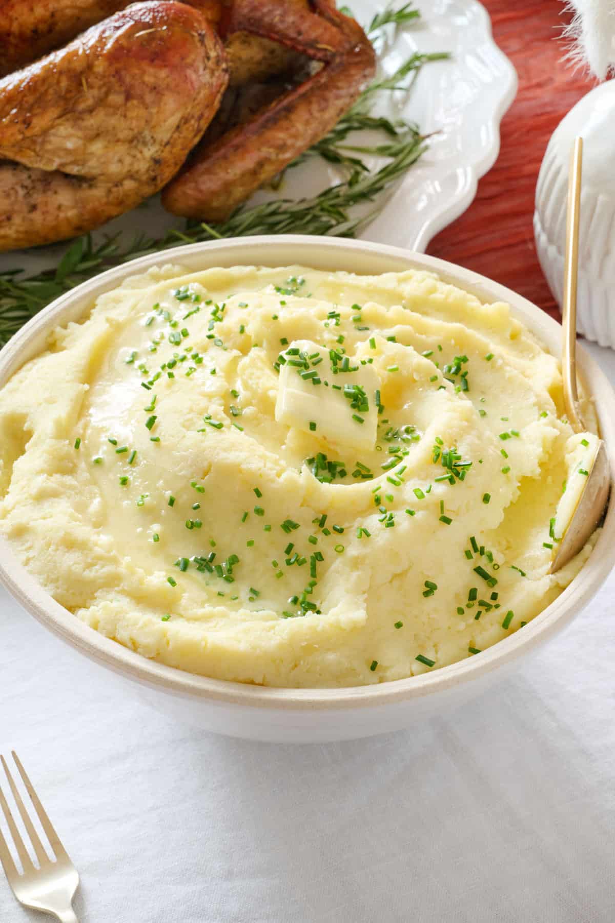 Classic mashed potatoes recipe in a serving bowl on dinner table with spoon dipped inside.