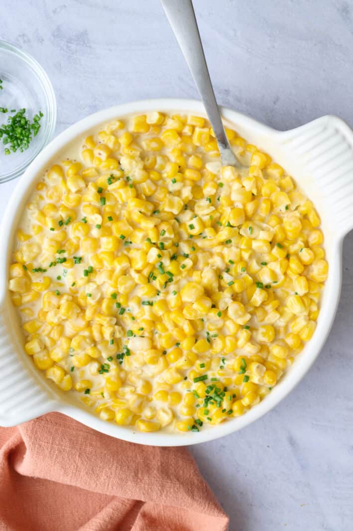Creamed corn in a serving bowl with a serving spoon dipped inside, garnished with chopped chives.