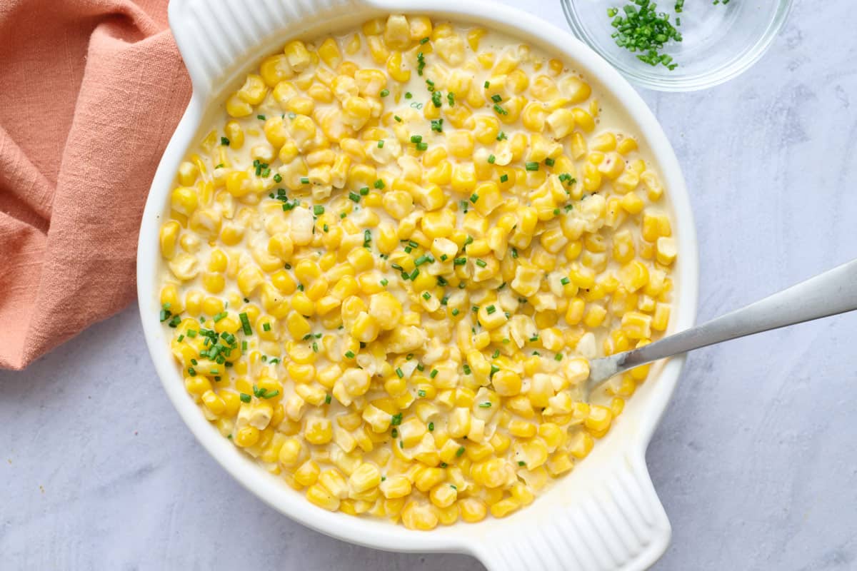 Creamed corn in a serving bowl with a serving spoon dipped inside, garnished with chopped chives.