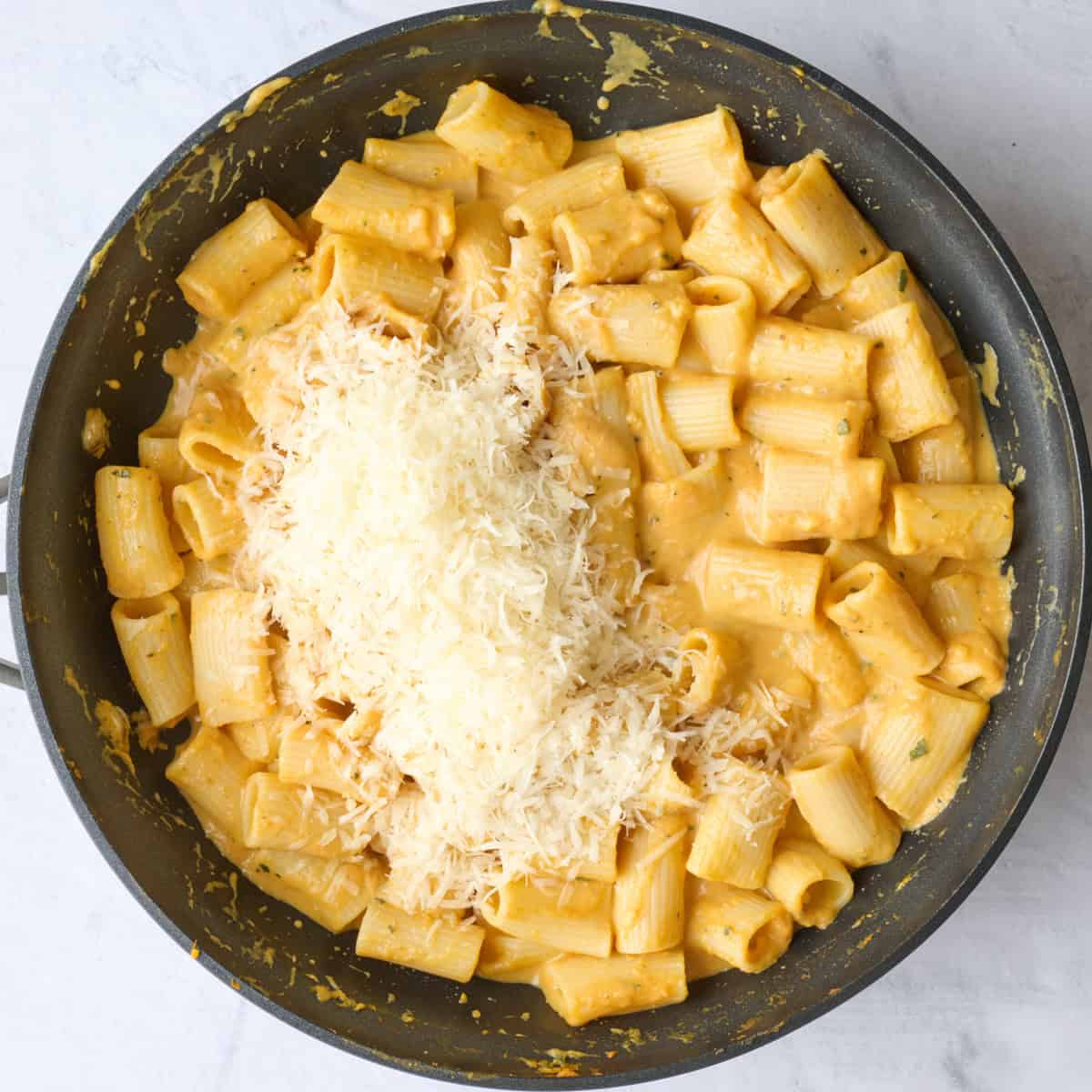 Freshly grated parmesan cheese added on top of pasta in skillet.