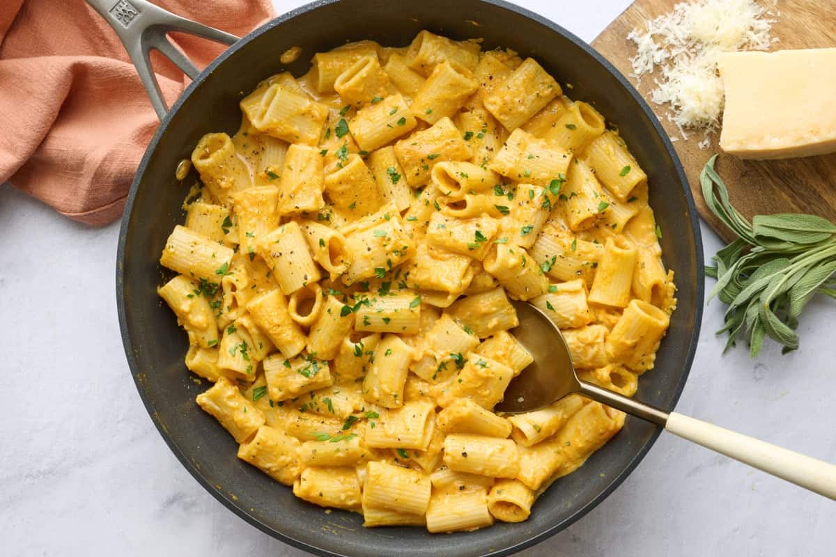 Homemade pumpkin pasta recipe in skillet. Grated cheese and fresh sage leaves are beside the skillet.