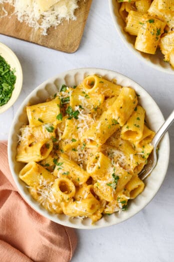 Creamy pumpkin pasta in a pasta bowl, garnished with parmesan and chopped parsley.