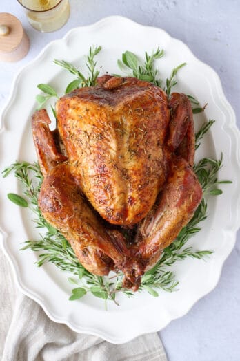 Whole dry brined turkey on a large platter on top of fresh herbs.