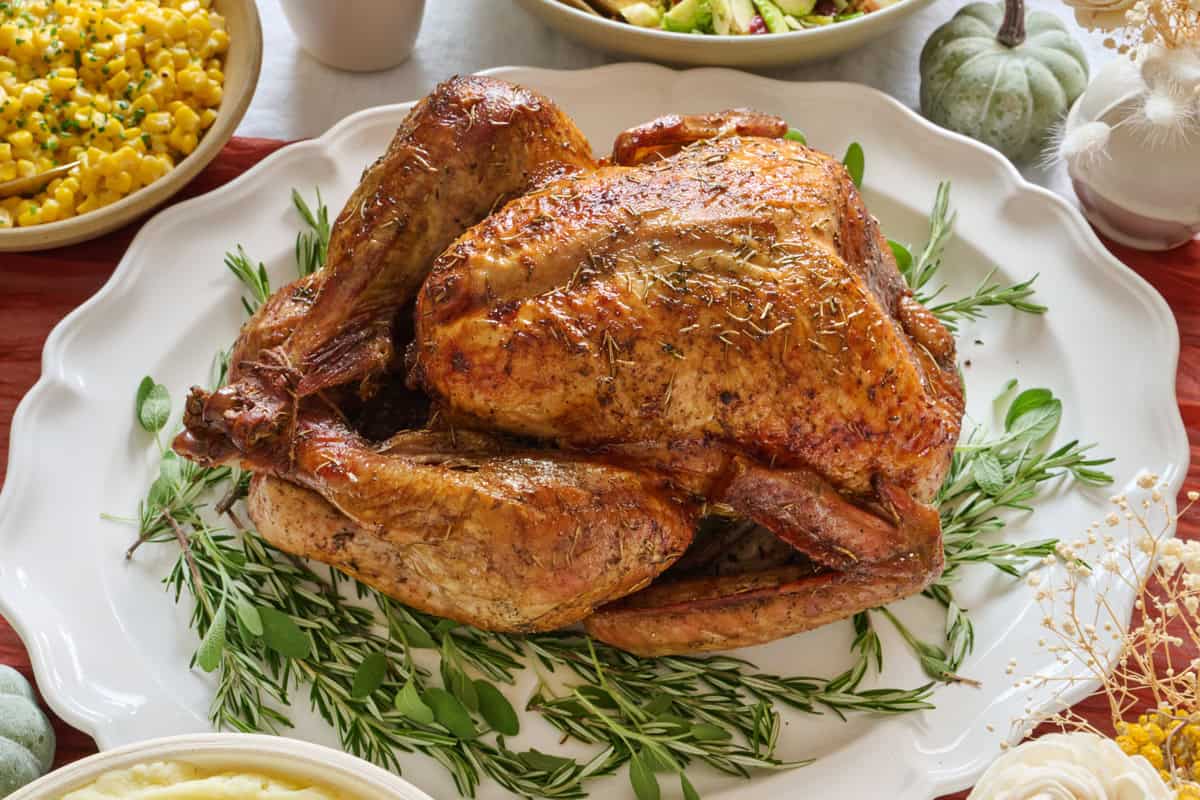 Whole roasted dry brined turkey on a platter with fresh herbs on thanksgiving table.