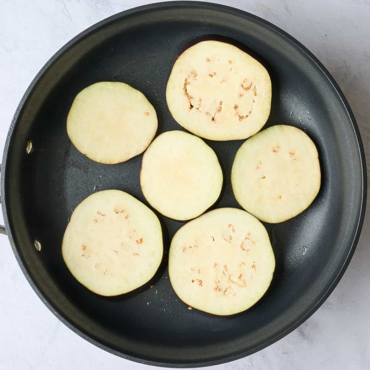 Eggplant slices in an oiled skillet.