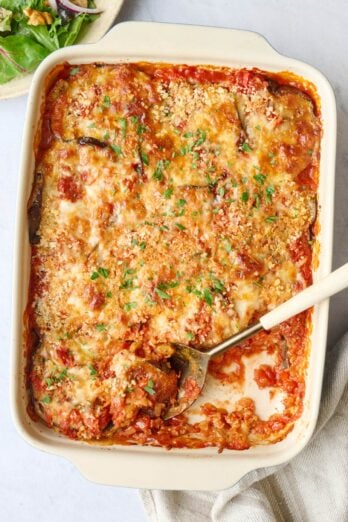 Eggplant casserole in baking dish with serving removed and serving spoon dipped inside.