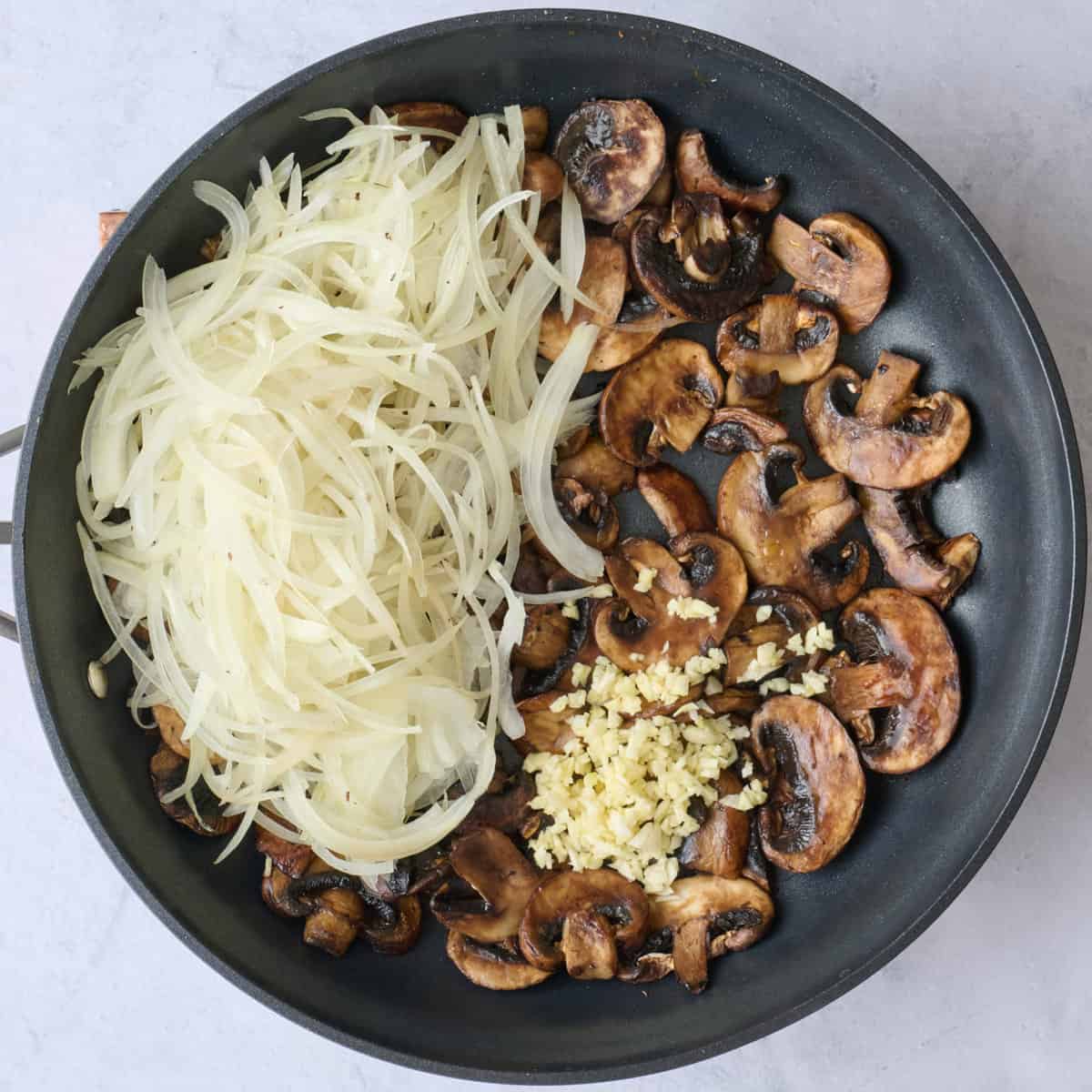 Thinly sliced onions and garlic added to pan with cooked mushrooms.