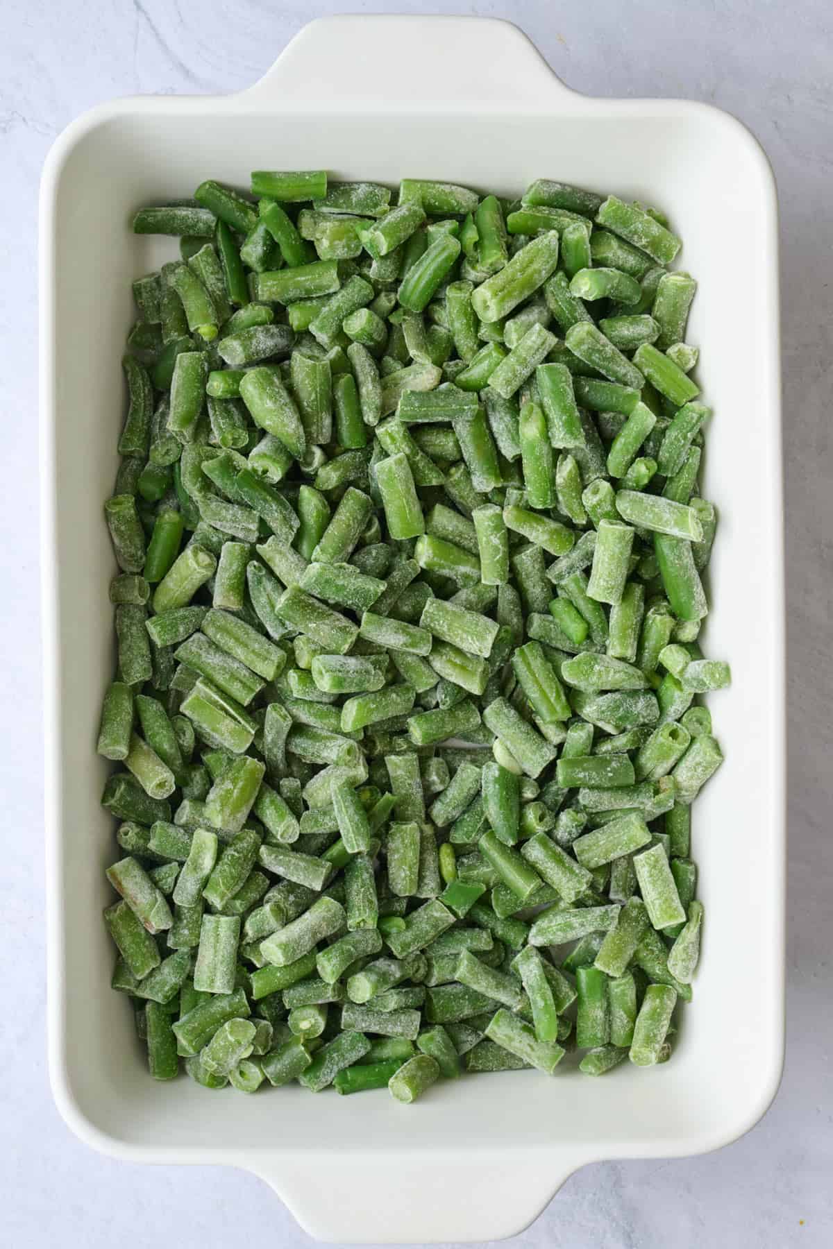 Frozen green beans added to a baking dish.