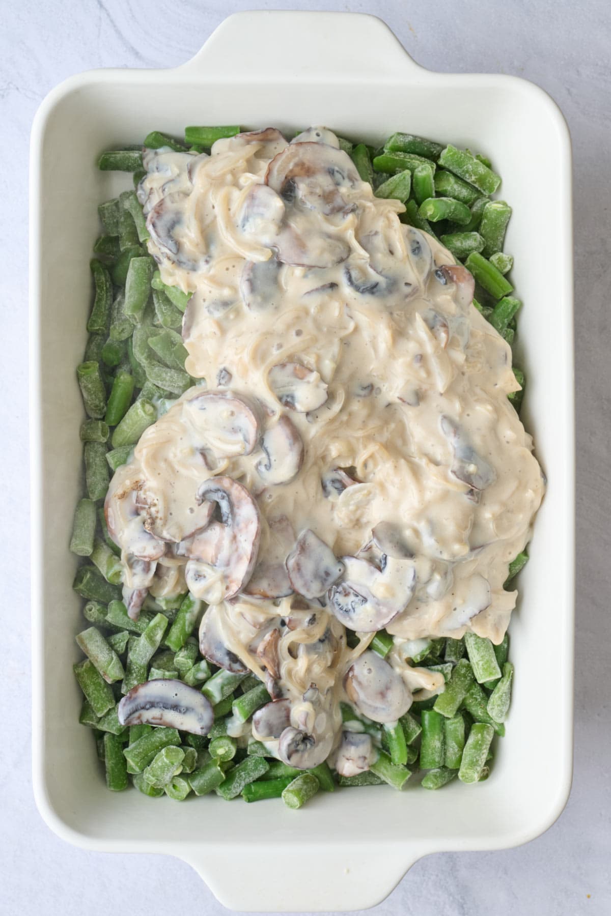 Mushroom cream sauce added on top of frozen green beans in a baking dish.