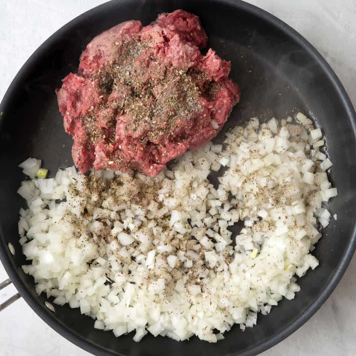 Ground beef, onions, and seasonings added to a large deep skillet before cooked.