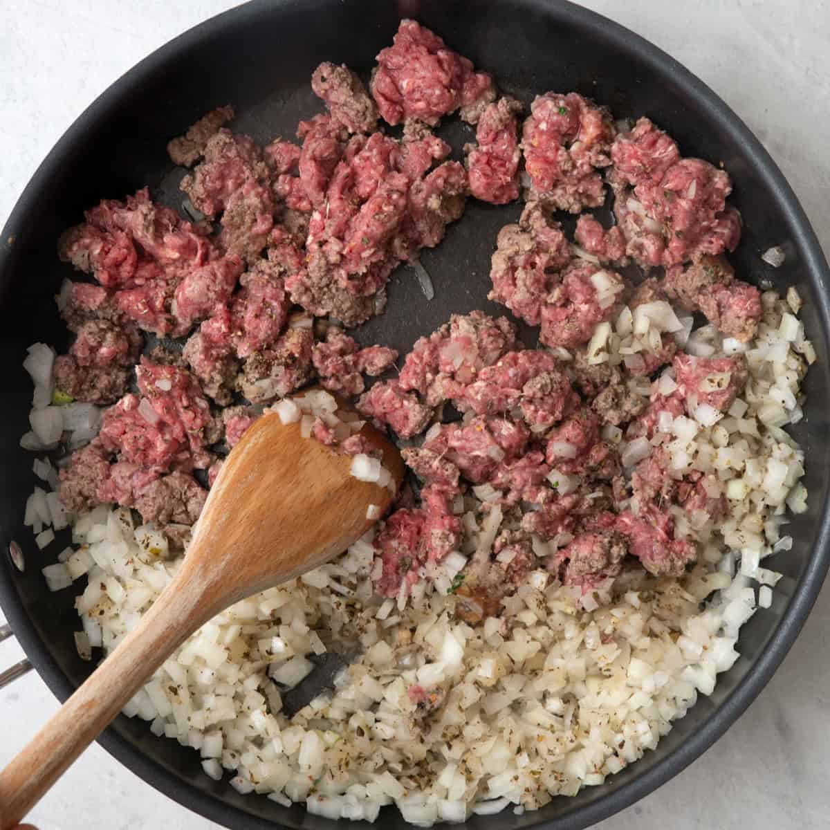 Wooden spoon breaking up the slightly cooked beef into smaller pieces.