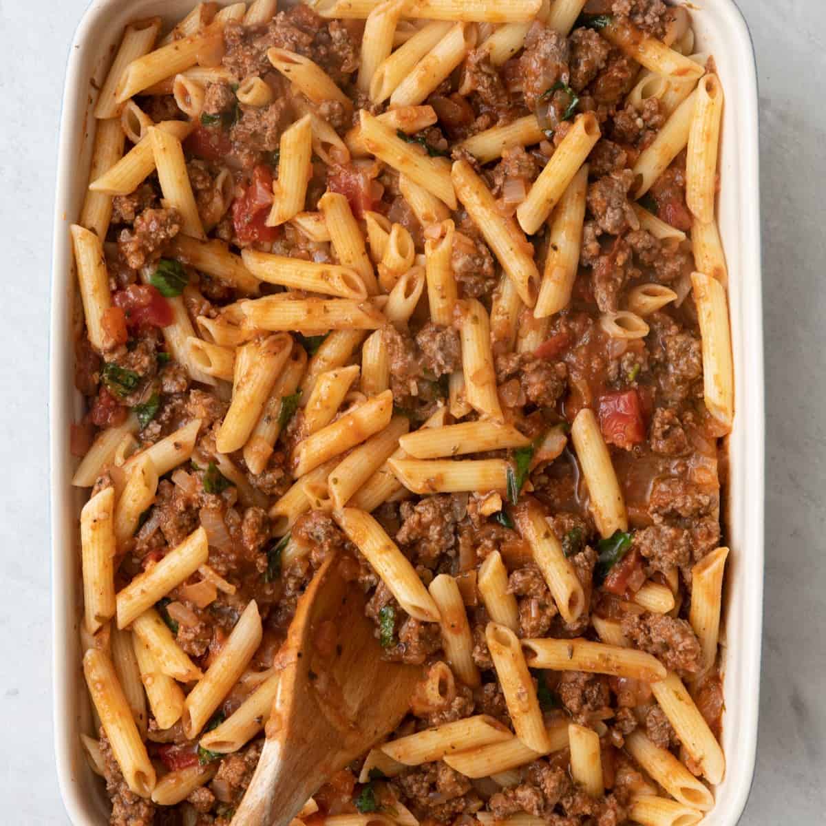 Beef mixture on top of cooked pasta in a baking dish.