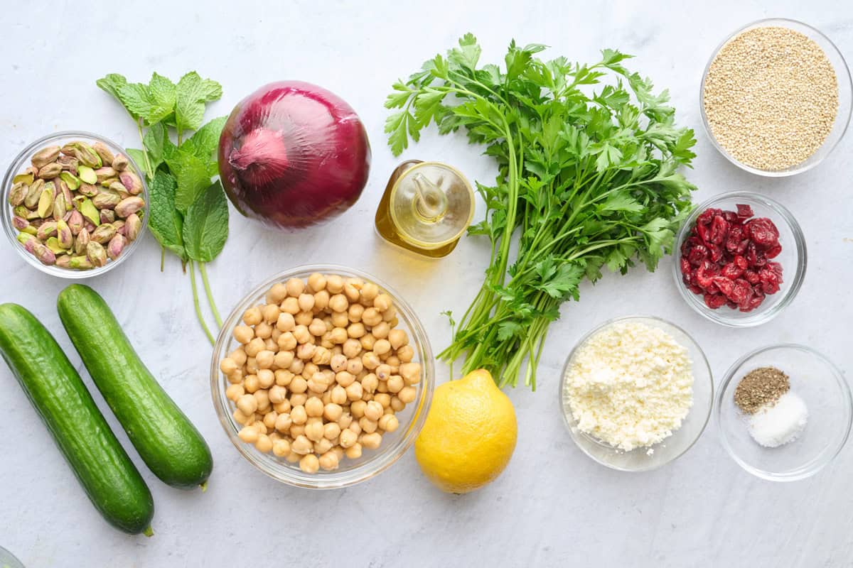 Ingredients for salad recipe: quinoa, oil, lemon, salt and pepper, chickpeas, red onion, pistachios, fresh parsley and mint, crumbled feta, and dried cranberries.