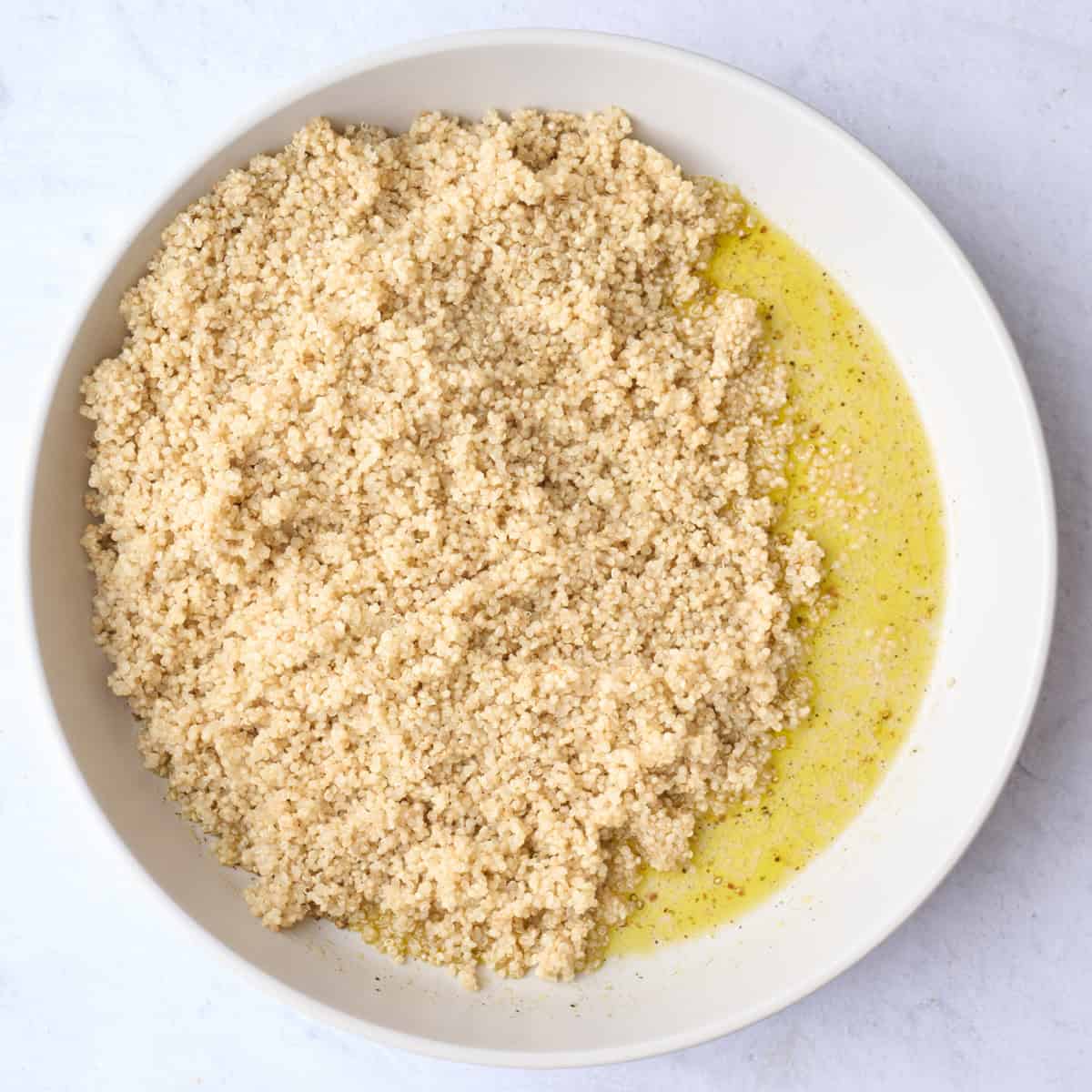 Cooked quinoa on top of dressing ingredients before tossing together.