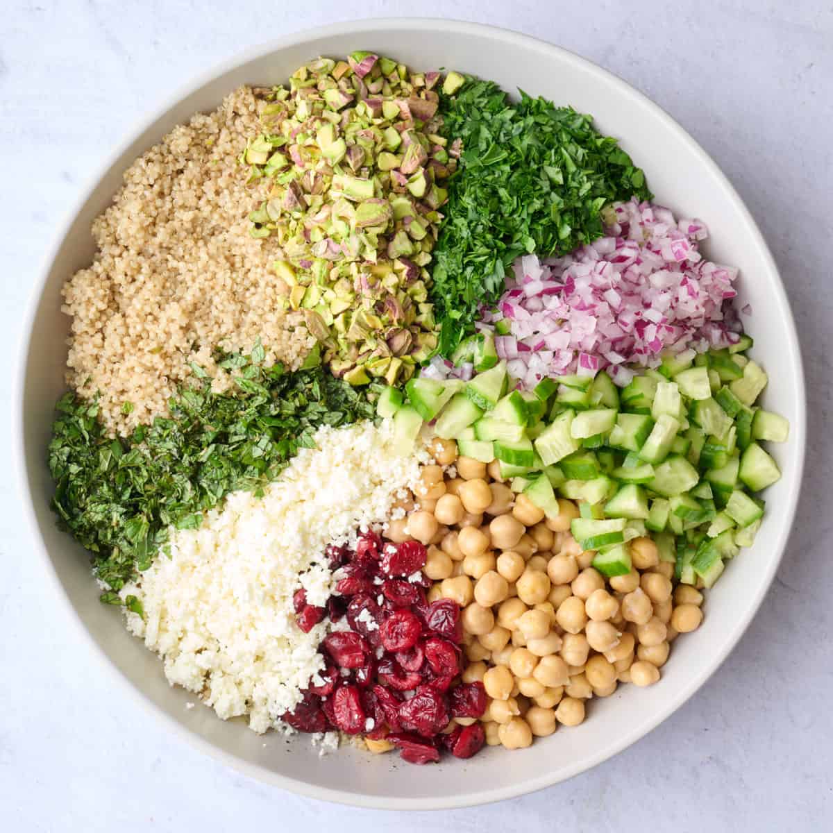 Cooke quinoa, chopped herbs and veggies, chickpeas, feta cheese and cranberries in a bowl before tossing together.