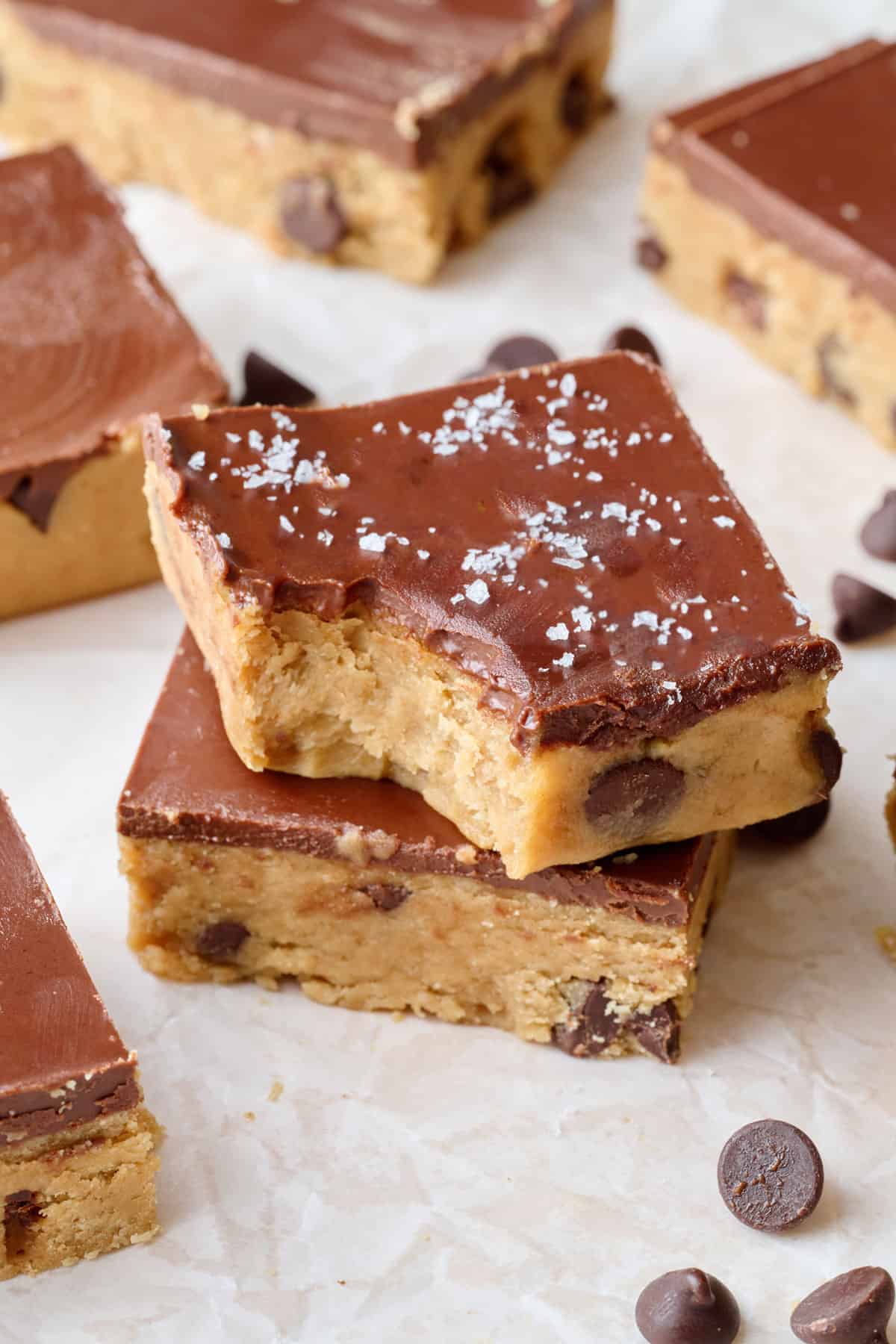 Chocolate chip no bake cookie dough bars on parchment, one with bite taken out with flaky salt on top.