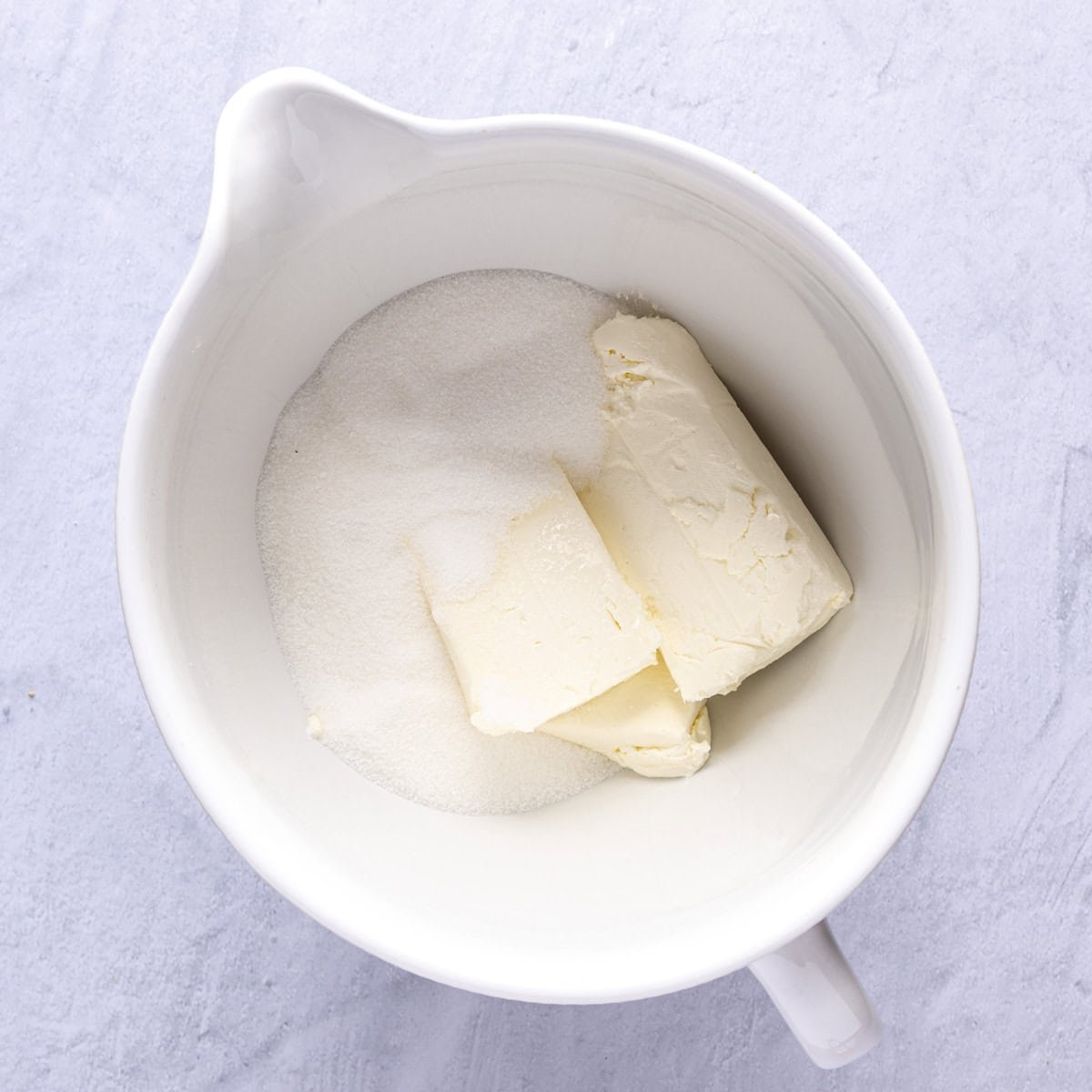 Cream cheese and sugar in bowl of stand mixer.