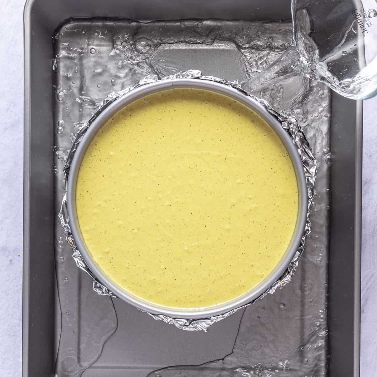 Cheesecake pan in a large roasting pan with water being poured in.