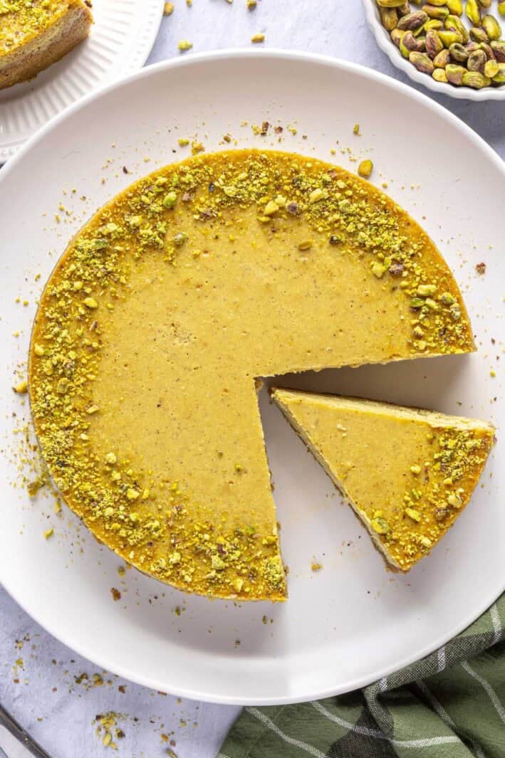 Baked pistachio cheesecake recipe on a platter with a slice cut out.