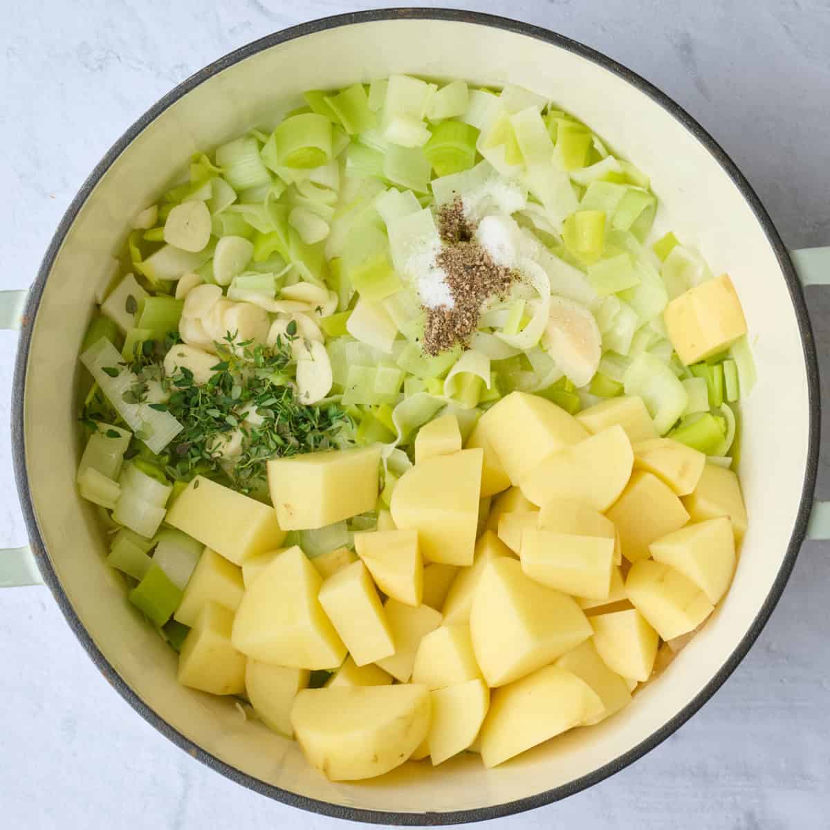 Chopped potatoes, leeks, garlic, and seasonings in a pot.