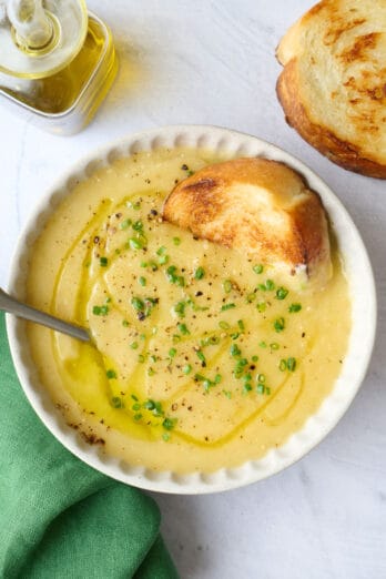 Bowl of creamy potato leek soup with bread dipped inside bowl.