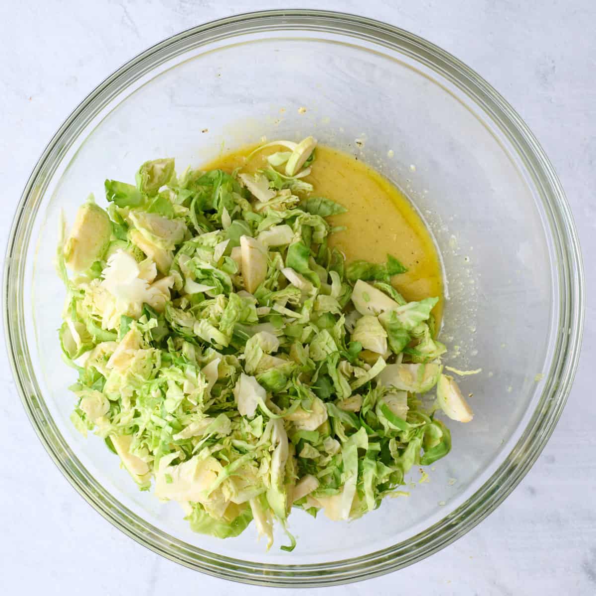 Dressing mixed in a bowl with shaved brussels sprouts on top.