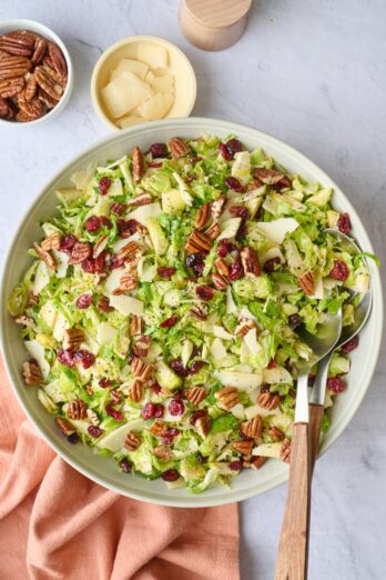 Shaved brussel sprouts salad in a serving bowls with fork and spoon serving set dipped inside.