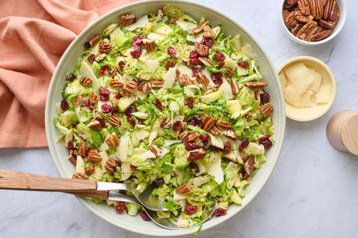 Shaved brussels sprouts salad in a serving bowls with fork and spoon serving set dipped inside.