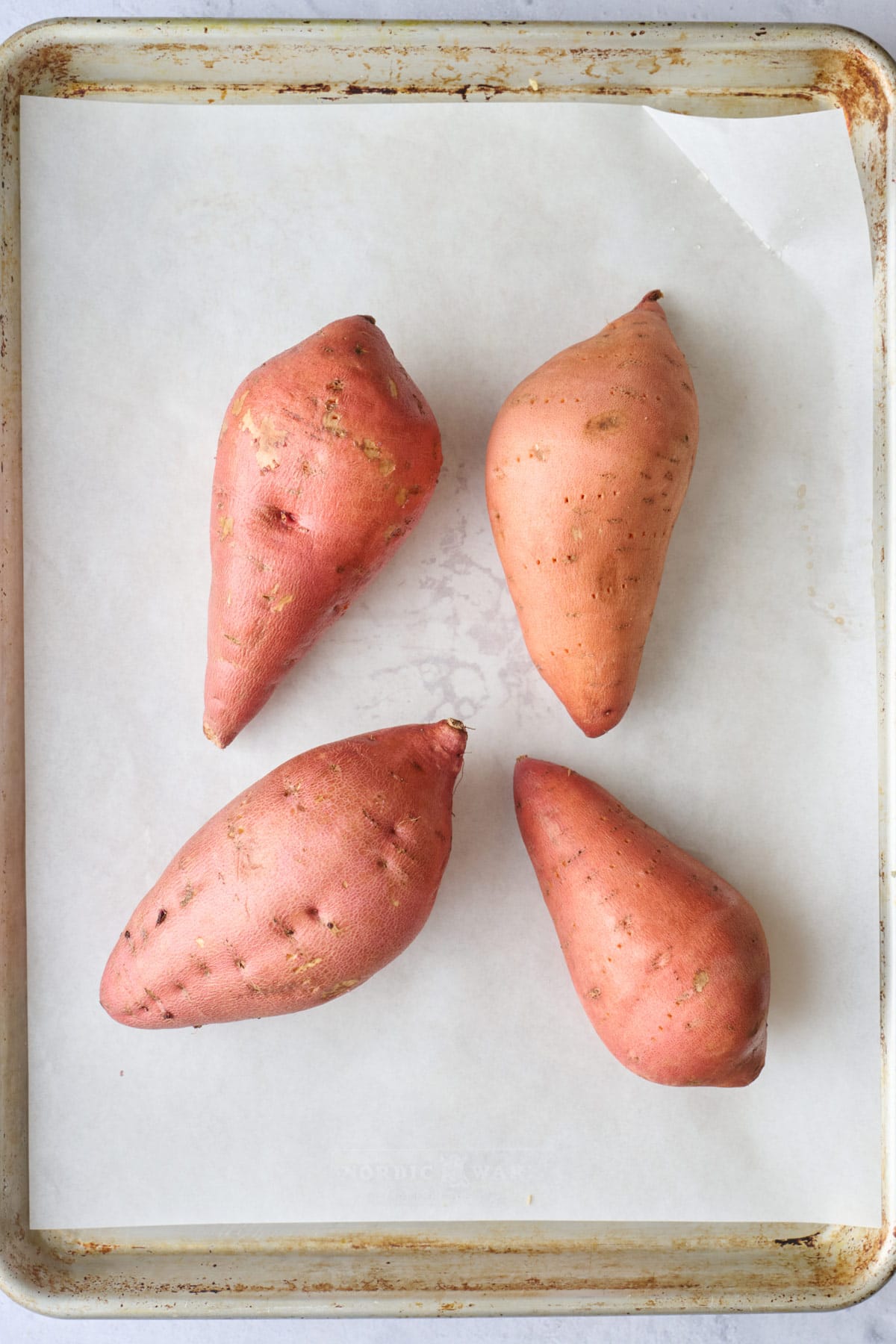 Sweet potatoes pierced with a fork on a parchment lined baking sheet before baking.
