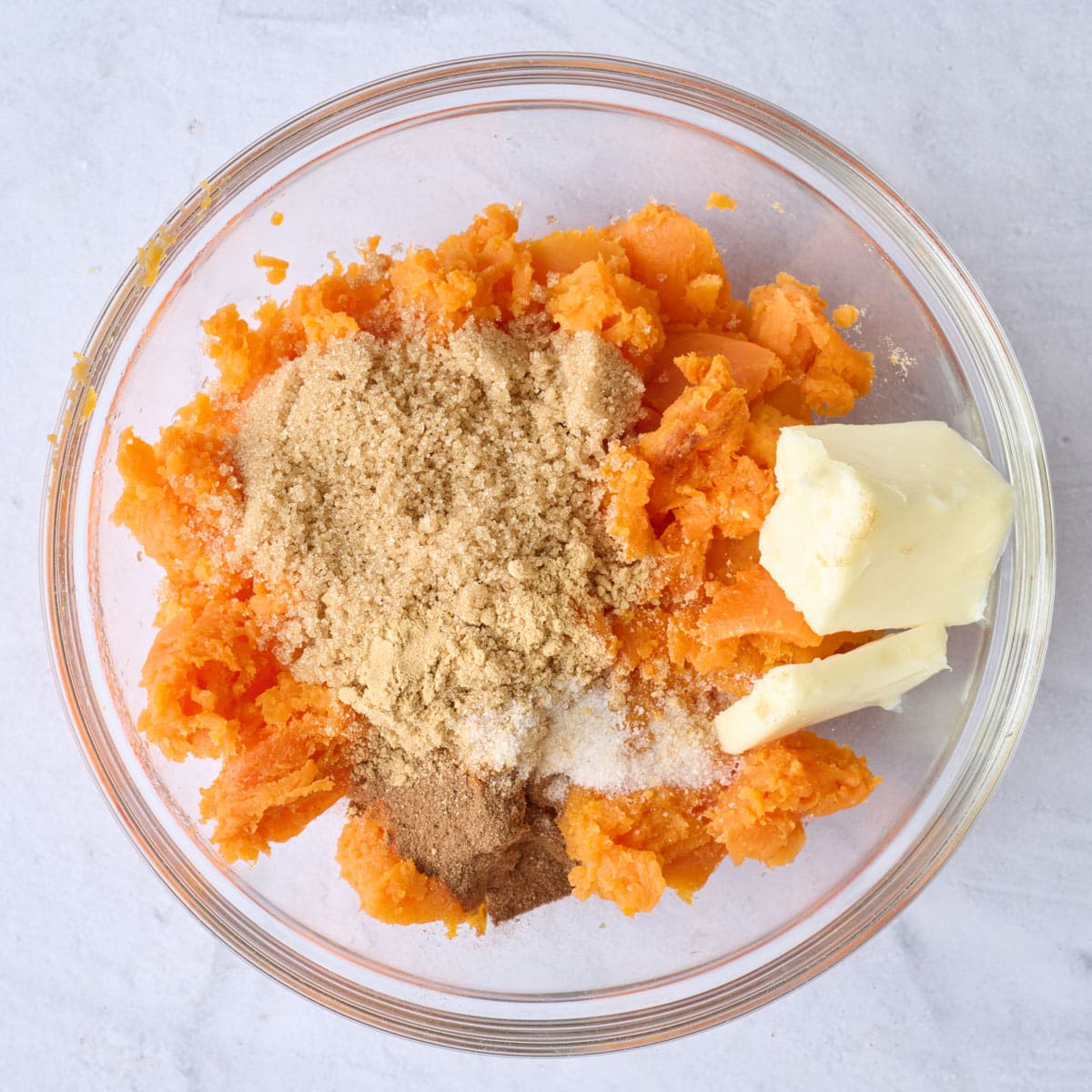 Potato flesh in a bowl with butter, brown sugar, and spices added before mixing.