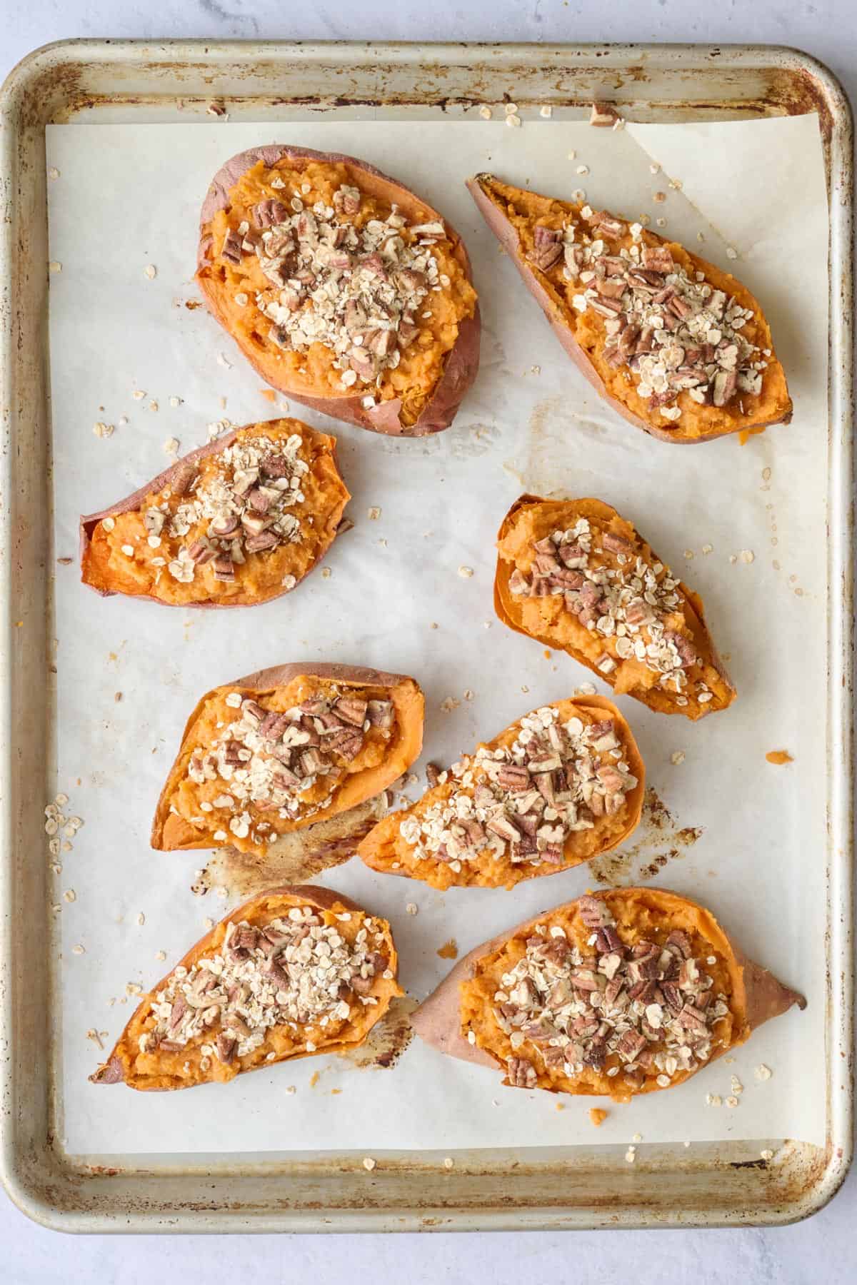 Sweet potato halves on a baking sheet filled with sweet potato mixture and topped with the pecan oat mixture.