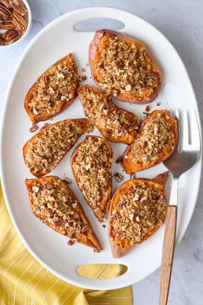 Twice baked sweet potatoes halves on a narrow platter with serving fork and small dish of chopped pecans.