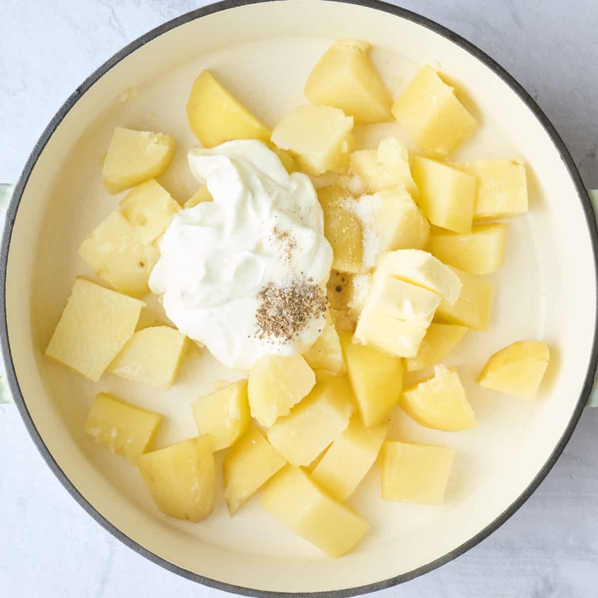 Cooked cubed potatoes in a pot with yogurt, butter, salt and pepper added.